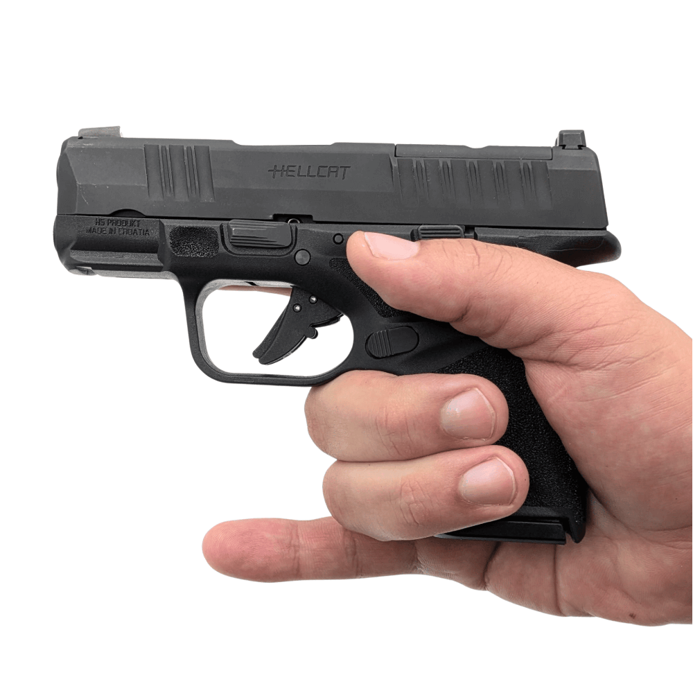 Springfield hellcat pistol in hand facing left with factory magazine that does not support the pinky.
